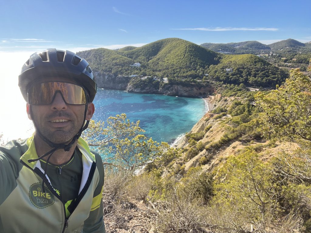 Fietser maakt een selfie boven een turquoise baai aan de kust van Ibiza